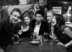 a group of people sitting at a table with beers in front of them and posing for the camera