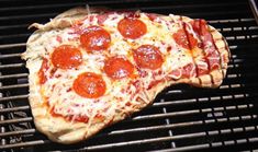 a pizza sitting on top of a grill covered in cheese and pepperoni