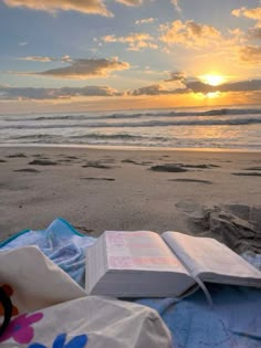 an open book sitting on top of a blanket next to the ocean