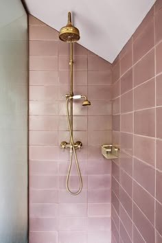 a pink tiled shower with gold faucet and hand held shower head in the corner