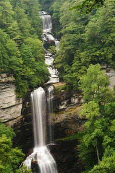 a waterfall surrounded by lush green trees and rocks