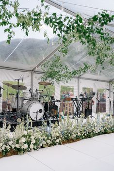 a band playing on stage under a tent with flowers and greenery in the foreground