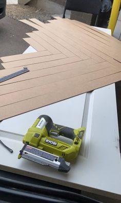 a cordless nailing machine sitting on top of a piece of plywood