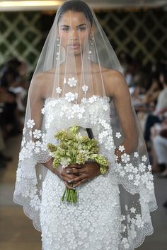 a woman in a white wedding dress holding a bouquet of flowers and wearing a veil