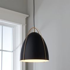 a black and gold pendant light hanging from a white wall next to a large window