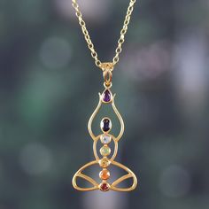 Chakras align by taking the form of seven faceted jewels held within a 22k gold-plated figure in a meditative pose. Indian artisan Alok Jain's pendant necklace conveys elegance and mysticism in its representation of the seven centers of spiritual energy, each portrayed by precious gems in a bezel setting. Red garnet depicts the foundational root chakra, with a carnelian stone above it for the sacral chakra, which relates to accepting change. Yellow citrine for the solar plexus chakra stands for confidence, and green peridot stands for the heart chakra and love. Blue topaz for communication sits in the throat chakra position, and the figure's head holds iolite for the focusing third eye chakra. The line is finished at the top with a purple amethyst, held aloft, representing the crown chakra Red Stone Jewellery, Meditative Pose, Accepting Change, Red Stone Jewelry, Teapot Necklace, Chakra Pendant, Chakra Necklace, Spiritual Energy, Carnelian Stone