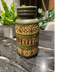 a green vase sitting on top of a table next to a potted plant in the background