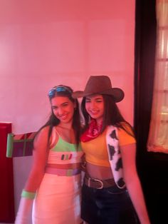 two young women standing next to each other in front of a pink wall wearing cowboy hats