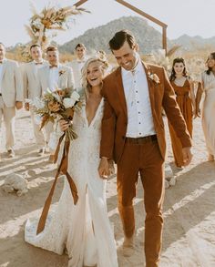 a bride and groom walking down the beach with their bridal party in the background