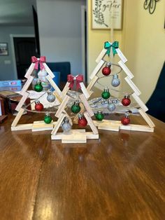 three wooden christmas trees with bells and bows on them sitting on top of a table