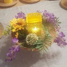 a basket filled with flowers and a lit candle on top of a white table cloth