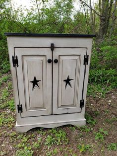 an old white cabinet with black stars painted on the doors and bottom is sitting in some grass