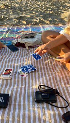 two people sitting on the beach playing with their cell phones and other electronic gadgets