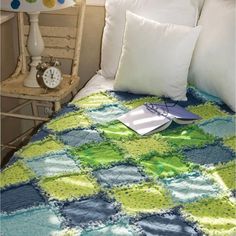 a bed with a green and blue quilt on top of it next to a chair