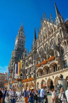 many people are walking around in front of an old building with towers and spires