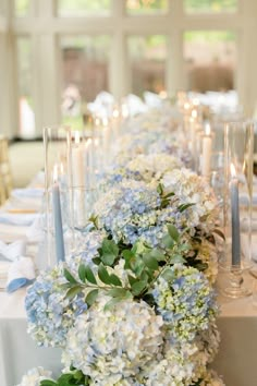 a long table with blue and white flowers, candles and napkins on top of it