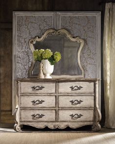 an old dresser with flowers in a vase on top of it and a mirror behind it