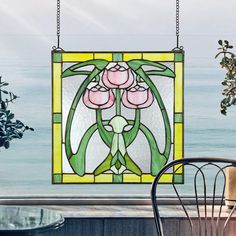 a stained glass window with flowers hanging from it's sides near a table and chair