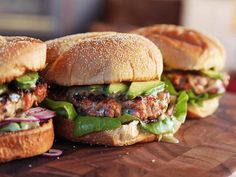 three hamburgers sitting on top of a wooden cutting board