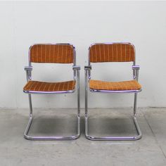 two chairs sitting next to each other on top of a cement floor in front of a white wall