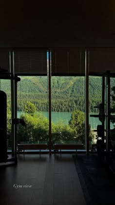 an empty gym room with large windows looking out onto a lake and mountains in the distance