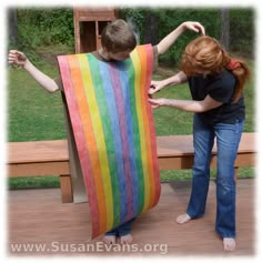 two children are holding up a rainbow colored blanket