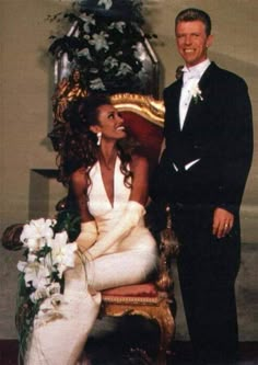 a man and woman posing for a photo in front of a chair with flowers on it