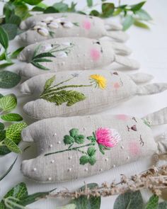 four embroidered flowers are lined up next to some green leaves and twigs on a white surface