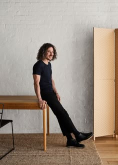 a man sitting on top of a wooden table next to a chair and bookcase