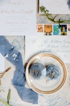 two wedding rings on a plate next to some blue and white paper with gold trim