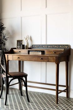 a wooden desk with a sign that says first class waiting room on it next to a chair and potted plant