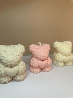 three small teddy bears sitting next to each other on a white counter top in front of a beige wall