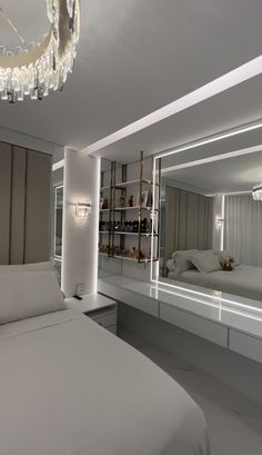 a large white bed sitting in a bedroom under a chandelier next to a mirror