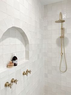 a white tiled shower with gold fixtures and soap dispenser on the wall