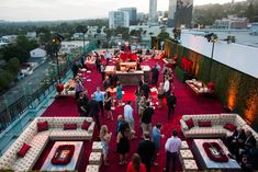 a group of people standing on top of a red carpet covered rooftop next to white couches