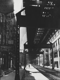 an old black and white photo of people walking under a train track in the city