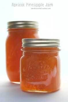 two mason jars filled with apricot pineapple jam on a white table top