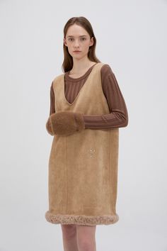 This Shearling Trimmed Suede Dress combines rustic elegance with modern design, making it a standout piece for the cooler months. Crafted from 90% suede and 10% polyurethane, the dress features a soft and luxurious texture, while the 100% shearling trim along the hem adds warmth and a tactile element to the overall look. Its relaxed A-line silhouette provides both comfort and a flattering fit, with the mini length adding a youthful, playful touch. Perfect for layering, this dress can be styled over a fitted turtleneck or paired with a cozy cardigan for a chic, autumn-ready look. The shearling trim not only enhances the dress’s warmth but also brings added texture and dimension. Complete the outfit with ankle or knee-high boots for an effortlessly stylish and versatile ensemble that transit Elegant Leather Winter Dresses, Elegant Winter Leather Dresses, Chic Brown Mini Dress For Winter, Elegant Leather Dresses For Winter, Chic Leather Winter Dress, Teddy Bear Coat, Chic Autumn, Fitted Turtleneck, Cozy Cardigan