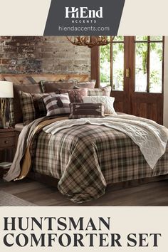 a bed with plaid comforter and pillows in front of a brick wall next to a window