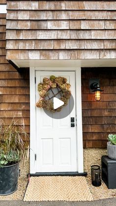 a white door with a wreath hanging on it's side next to potted plants