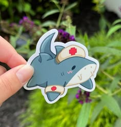 a hand holding up a sticker with a shark on it's back and red eyes