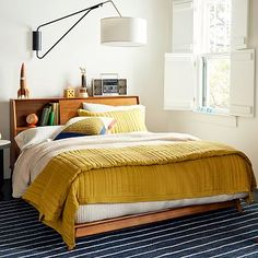 a bed with yellow blankets and pillows in a bedroom next to a window that reads west elm