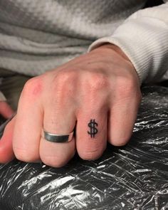 a person's hand with a ring on it and a dollar sign tattooed on the middle finger