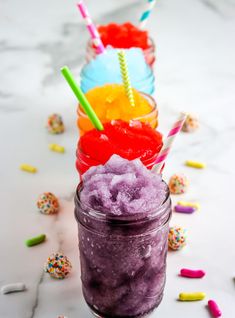 three glasses filled with different colored drinks on top of a white table next to confetti and sprinkles