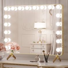 a vanity mirror with lights on it and flowers in vase next to it, sitting on a dresser