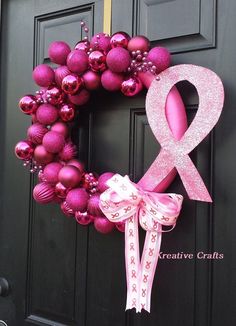 a pink ribbon is attached to a wreath on the front door with ornaments around it