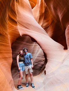 a man and woman standing in the middle of a slot at antelope canyon