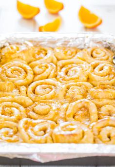 a pan filled with cinnamon rolls on top of a wooden table next to sliced oranges