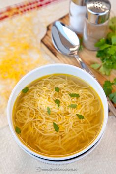 a bowl of soup with noodles and parsley on the side next to a spoon