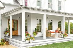 a white house with lots of flowers on the front porch and covered in wood furniture